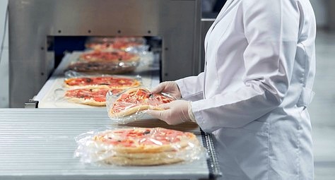 Worker inspecting pizzas on a factory packaging line