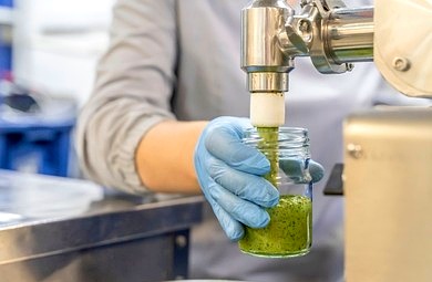 Pesto sauce being dispensed into a glass jar