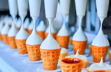 Soft-serve ice cream being filled into cones on a production line.